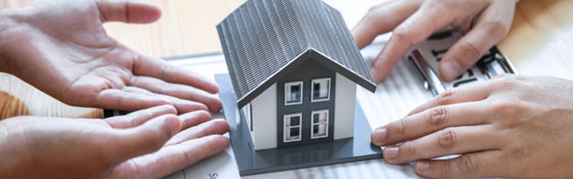 Immobilienverkauf nach Scheidung - Achtung Steuerfalle! Zwei Personen tauschen ein Modellhaus über einem Dokument aus, was eine Immobilienübertragung oder einen Hauskaufvertrag symbolisiert.