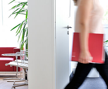 ECOVIS RTS Header Bild Standortseiten Frau im Büro mit ECOVIS Ordner rot unter dem Arm