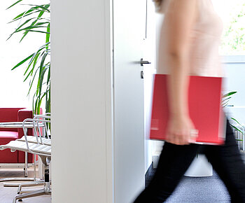 ECOVIS RTS Header Bild Standortseiten Frau im Büro mit ECOVIS Ordner rot unter dem Arm