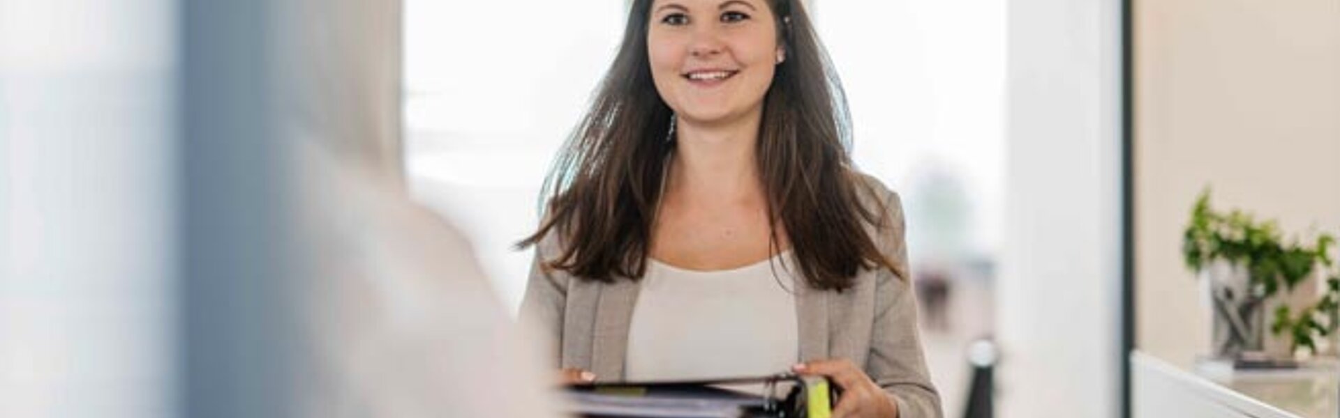 Vermeidung von Scheinselbstständigkeit bei Bürokräften Frau lächelt und hält einen Ordner in den Händen
