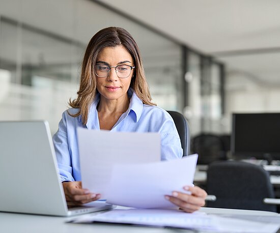 Frau mit Dokumente und Laptop am Schreibtisch