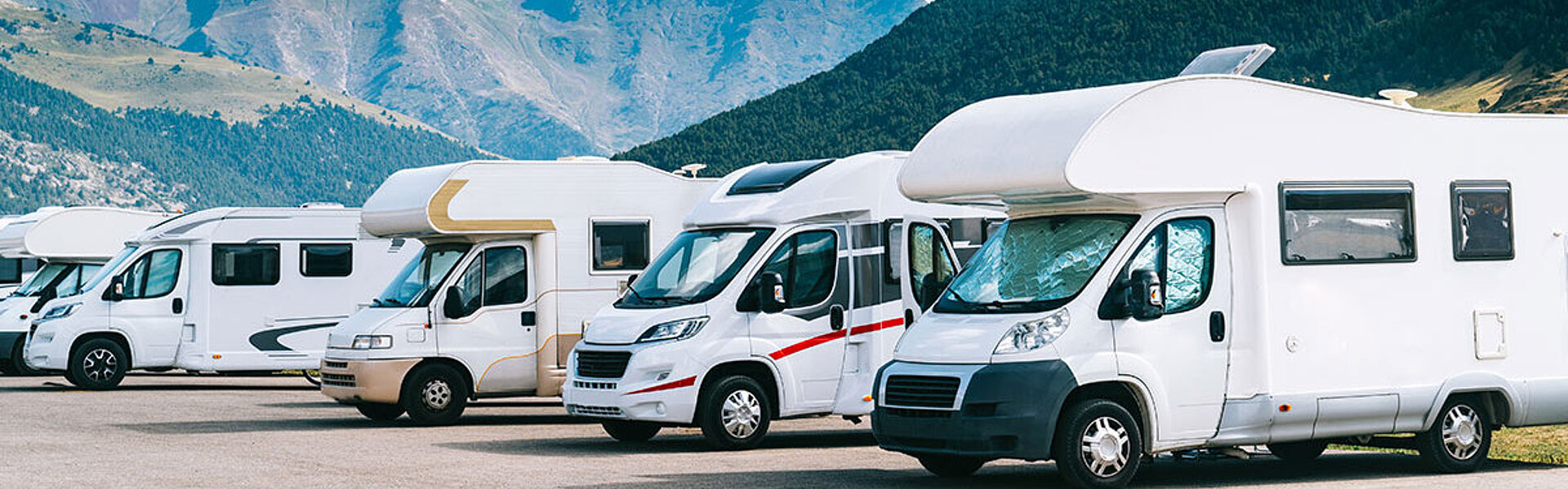 Steuerliche Fragen rund ums Wohnmobil Wohnmobile auf einem Parkplatz vor der beeindruckenden Kulisse der Berge